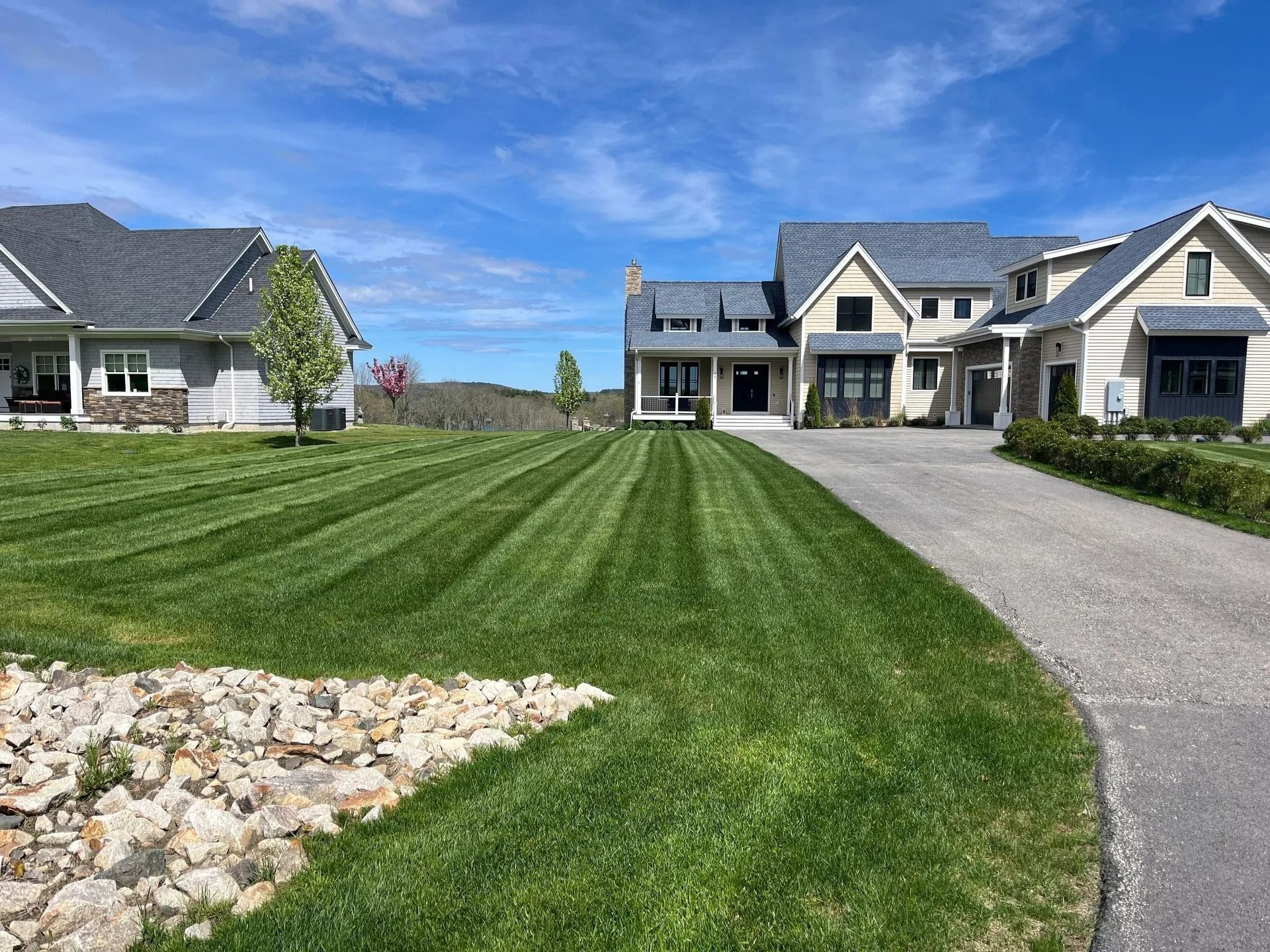 Lawn with striped pattern leading to a large house on a sunny day with blue sky. Other houses visible.