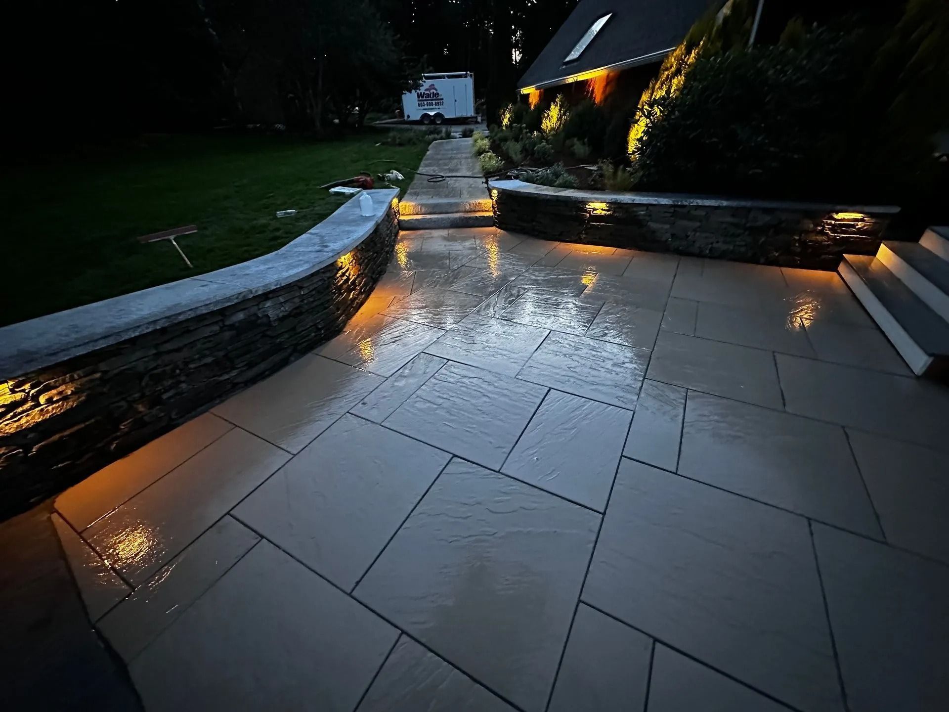 Lit stone patio and walls at night, with accent lighting reflecting off wet surface.