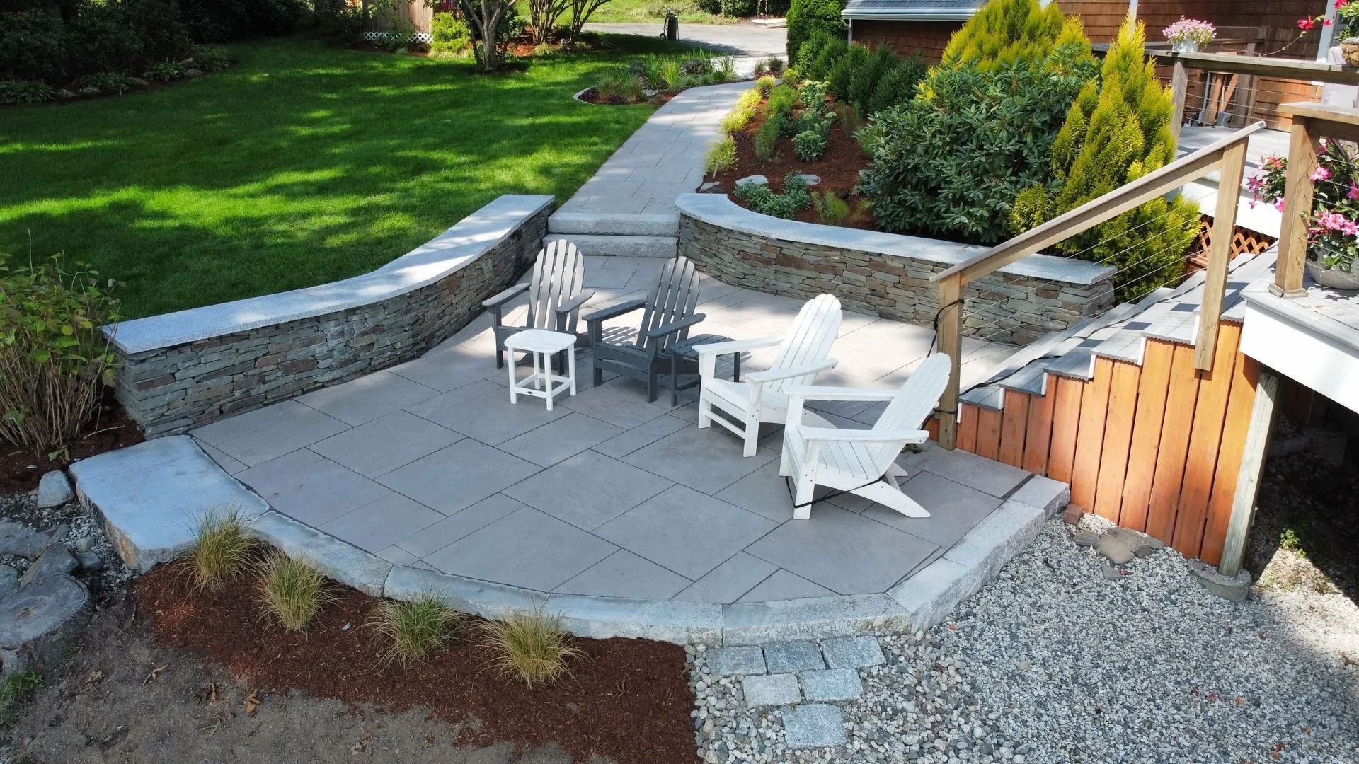 Stone patio with Adirondack chairs, low walls, and a pathway leading to a deck.
