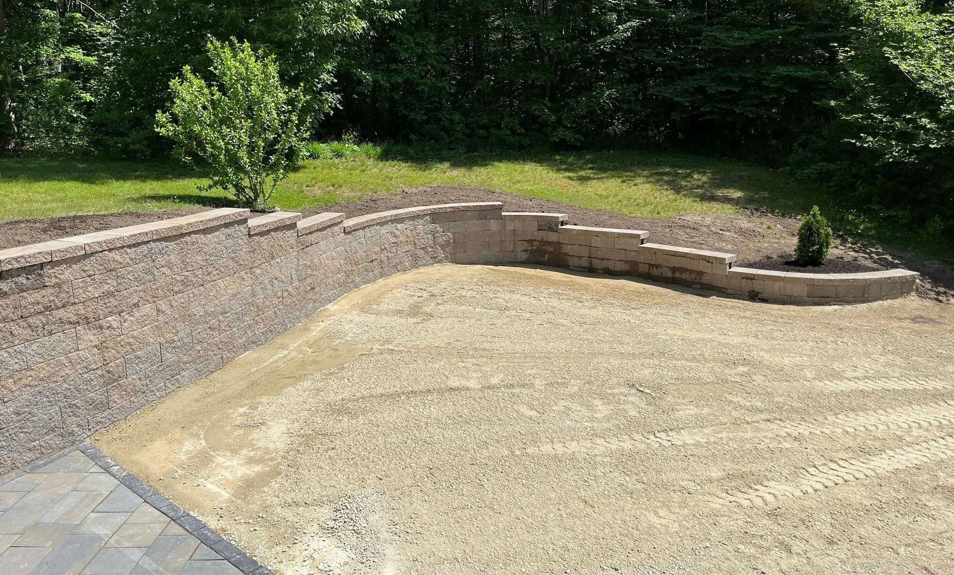 A gravel-covered yard is enclosed by a stone retaining wall. Green trees form the backdrop.