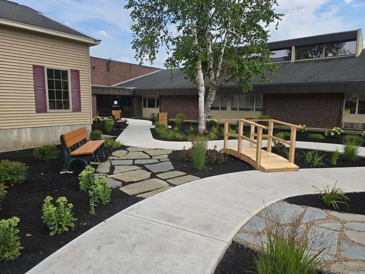 Courtyard with pathway, wooden bridge, garden beds, and building.