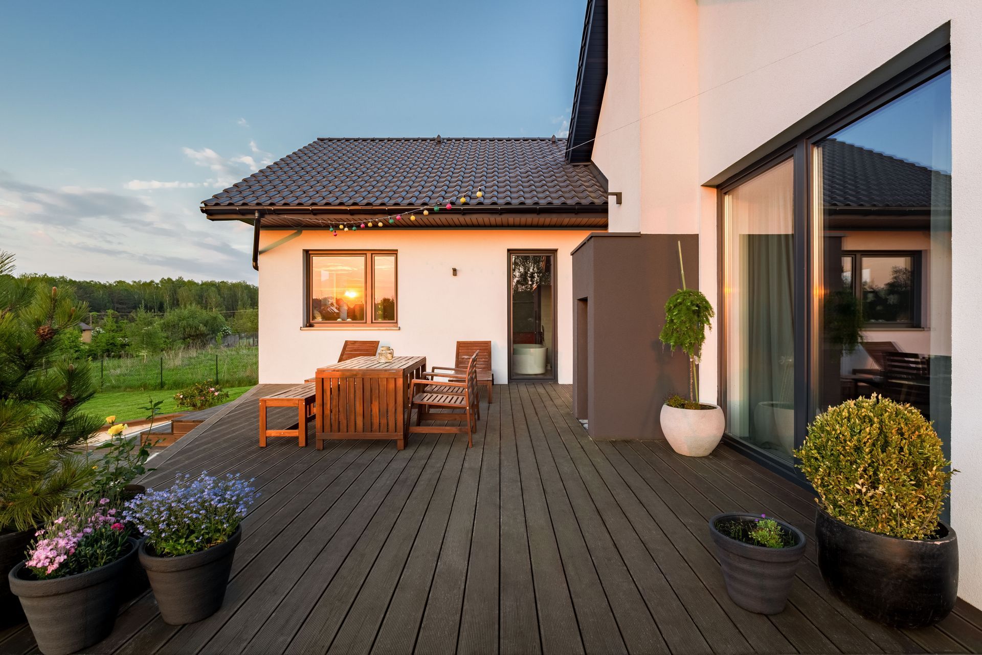 Modern patio deck with outdoor dining set beside a white house at sunset.