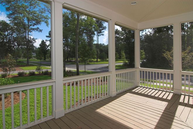 Covered porch with white railings, wooden floor, and sunlight overlooking a green yard and trees.