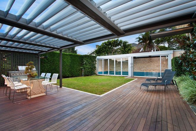 Covered wooden deck with outdoor dining table, lounge chairs, and a small lawn beside a garden wall.
