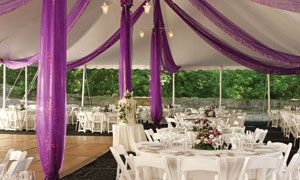 Purple-draped event tent with white tables and chairs set for an outdoor reception
