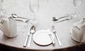 Elegant white table setting with plates, silverware, wine glasses, and folded napkins on a round table