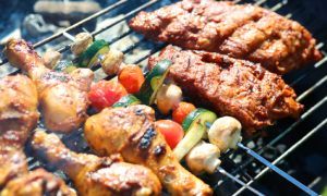Grilled chicken and vegetables sizzling on a barbecue rack, with char marks and glowing coals visible