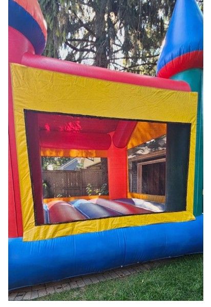 Colorful bouncy castle with red, yellow, and blue inflatable panels and mesh windows, set on a grass lawn.
