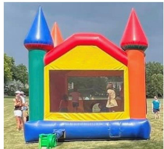 A multi-colored inflatable bounce house on a grassy field with children jumping inside and people standing nearby.