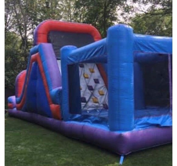 A blue, purple, and orange inflatable obstacle course and slide set up on a grassy lawn.