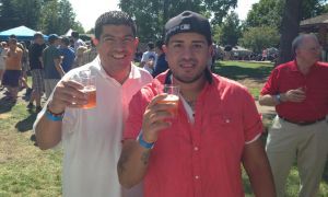 Two smiling people in colorful shirts holding drinks outdoors at a sunny gathering