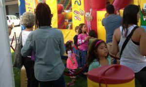 People gathered near a colorful booth; a child stands by a red table in a lively indoor event.