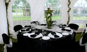 Black-and-white decorated banquet table under a white tent, set for an event with floral centerpiece