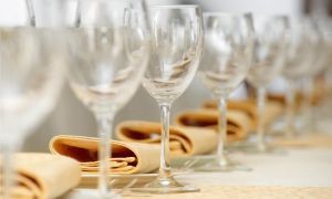 Wine glasses lined up with folded beige napkins on a table, set for a formal event