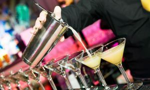 Bartender pouring a cocktail into martini glasses on a bar tray