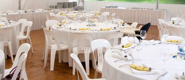Round banquet hall with white-clothed tables, white chairs, and yellow napkins set for an event.