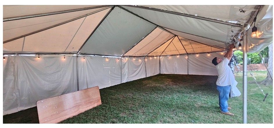 Large white tent interior with a grassy floor, tarp walls, and a person adjusting the side near the entrance
