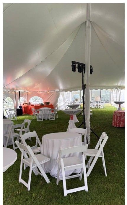 White event tent with round tables, folding chairs, and red couches on grass at an outdoor gathering.