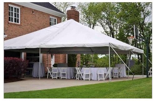 Large white event tent set up on a lawn beside a brick house with white tables and chairs inside.