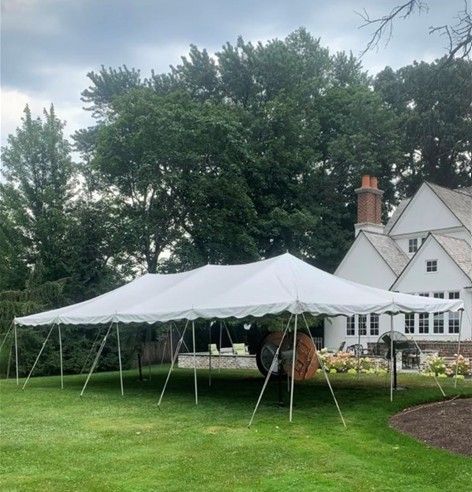 Large white event tent on a grassy lawn beside a white house and tall trees.