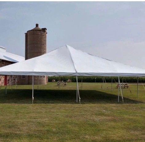 White canopy tent on a grassy field near a round silo and barn under a cloudy sky.