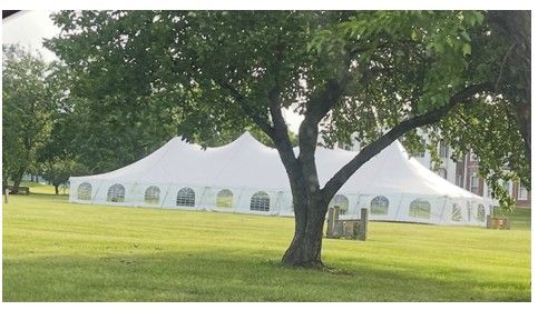 White event tent on a grassy lawn beneath trees in a park.