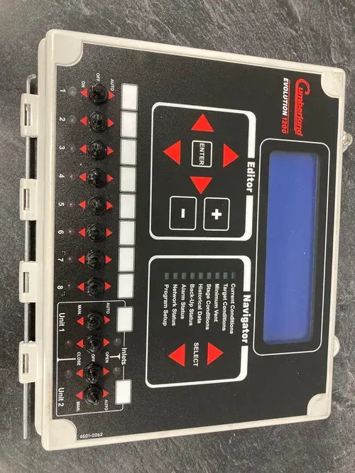 Black electronic control panel with blue display, red buttons, and rows of switches on a beige case