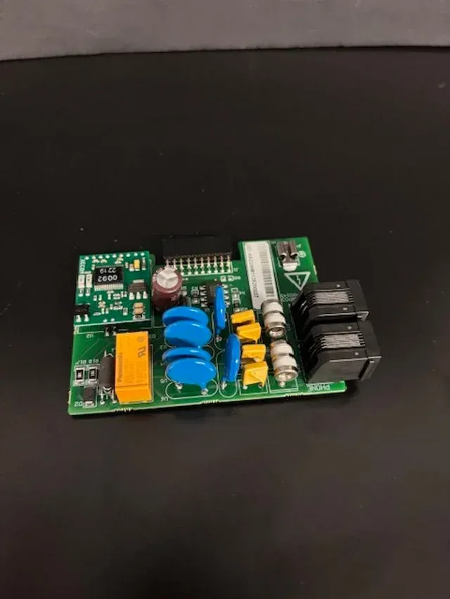 Small green circuit board with blue, yellow, and black components on a dark surface