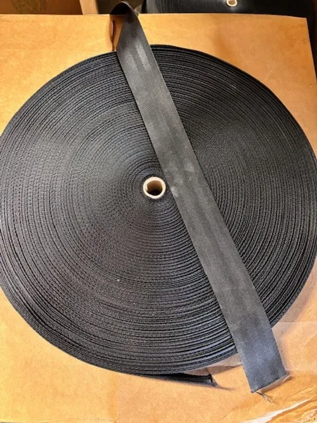 Coiled black strap with a central hole, wrapped diagonally on a tan surface.