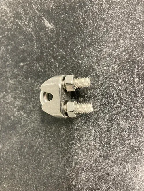 Small metal cable clamp with two threaded bolts on a dark textured surface