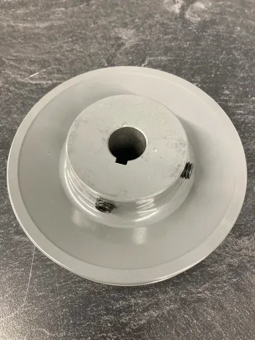 White circular metal component with a central hole on a gray textured surface