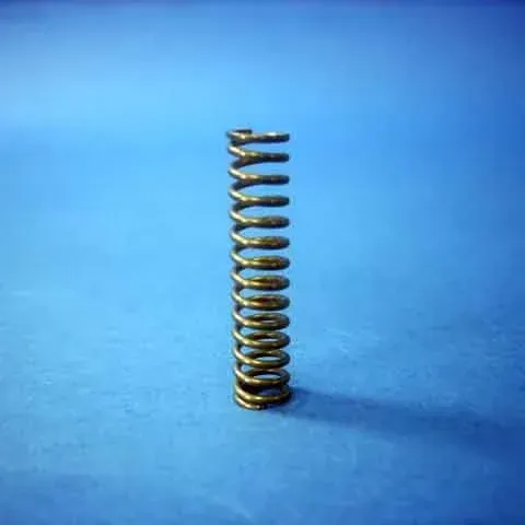 Small metal compression spring standing upright on a blue surface.