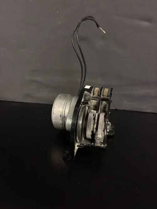Small metal mechanical part with a curved black wire on a dark surface
