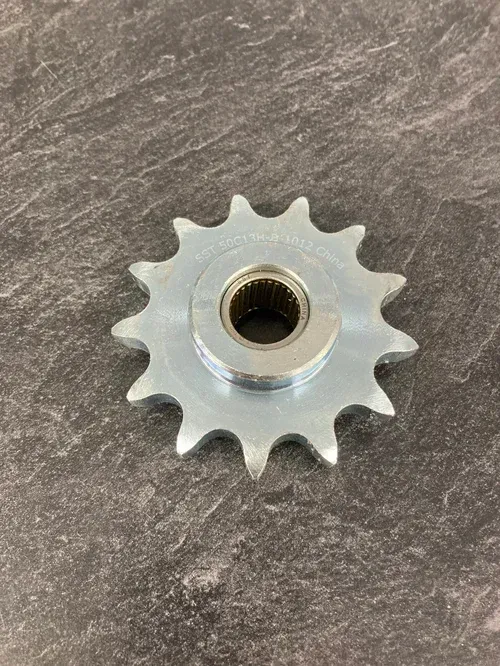 Silver metal sprocket gear with a threaded center hole on a gray stone surface