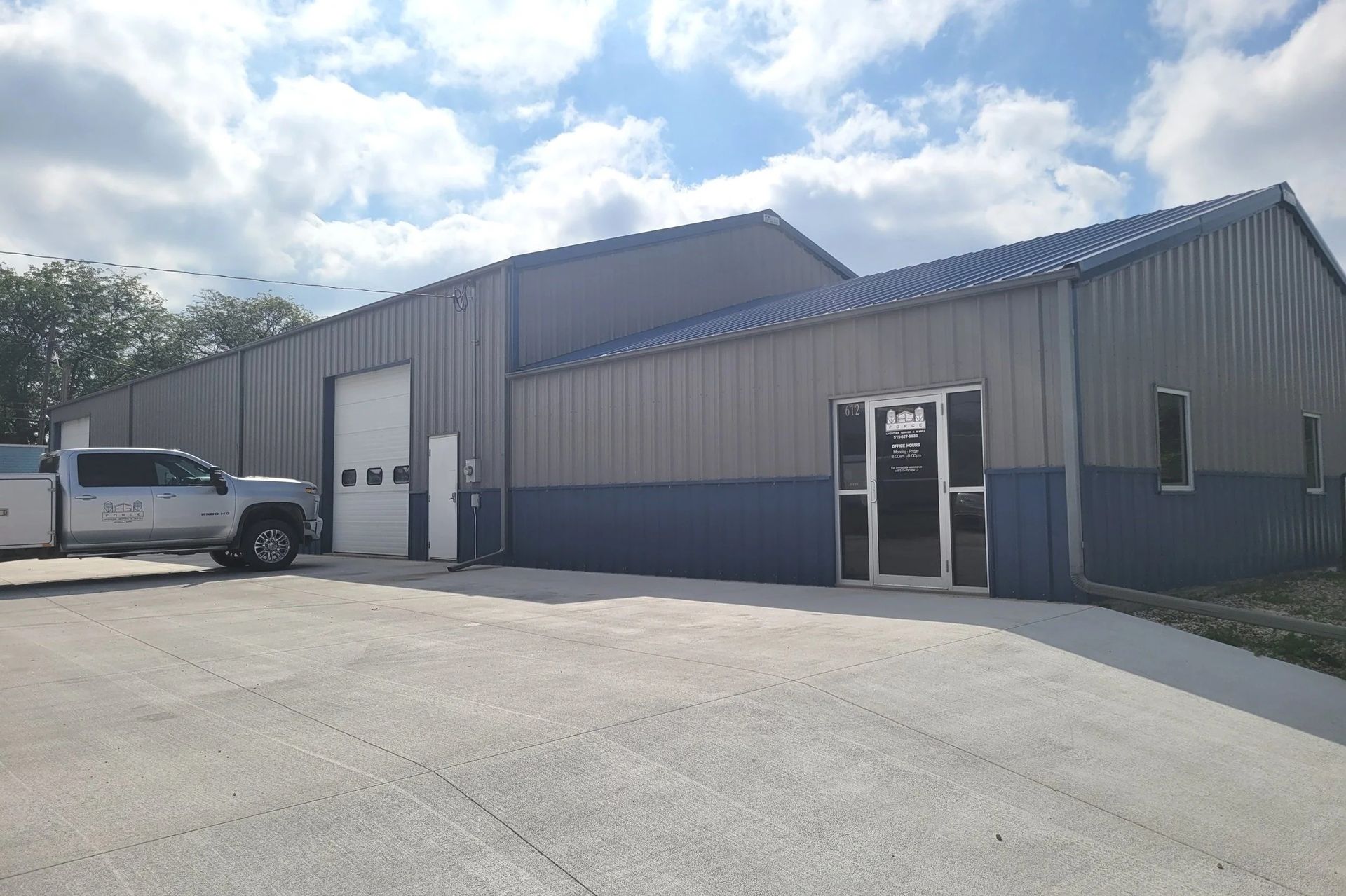 Gray metal warehouse with a white van parked outside under a partly cloudy sky