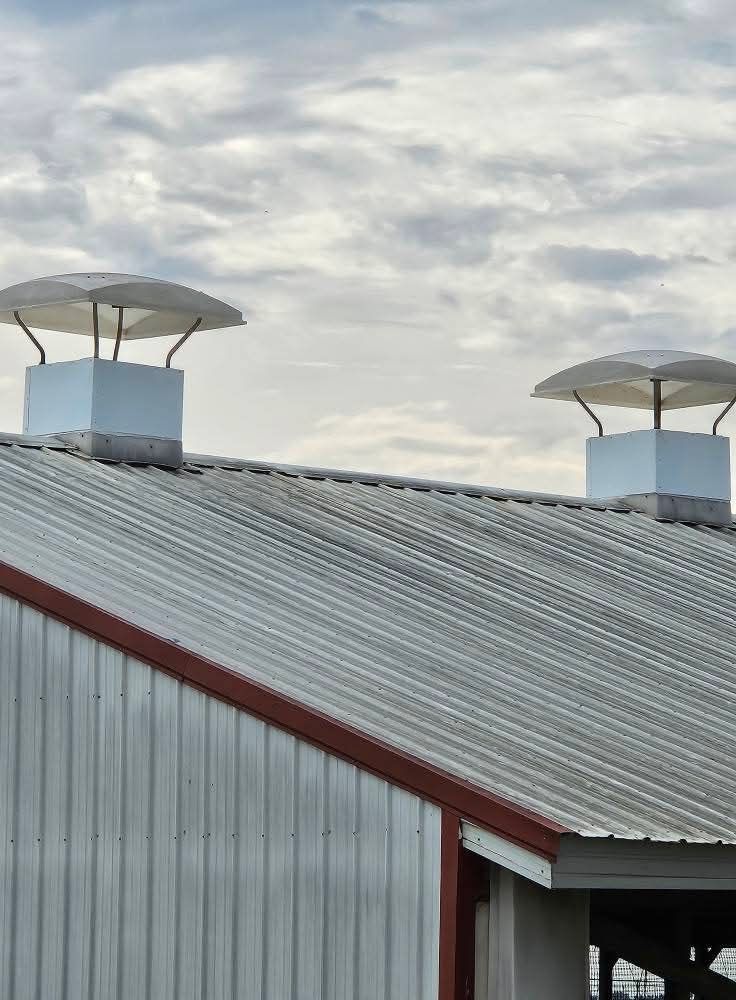Two rooftop vents on a corrugated metal roof under a cloudy sky