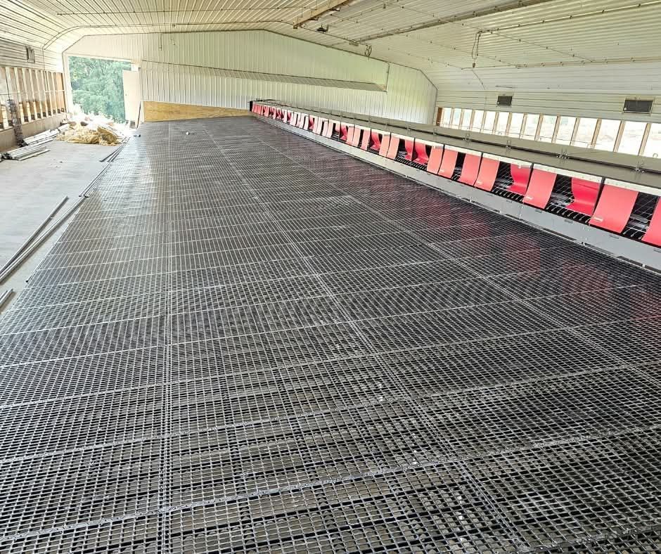 Large indoor construction area with a steel mesh floor and red barriers along one side