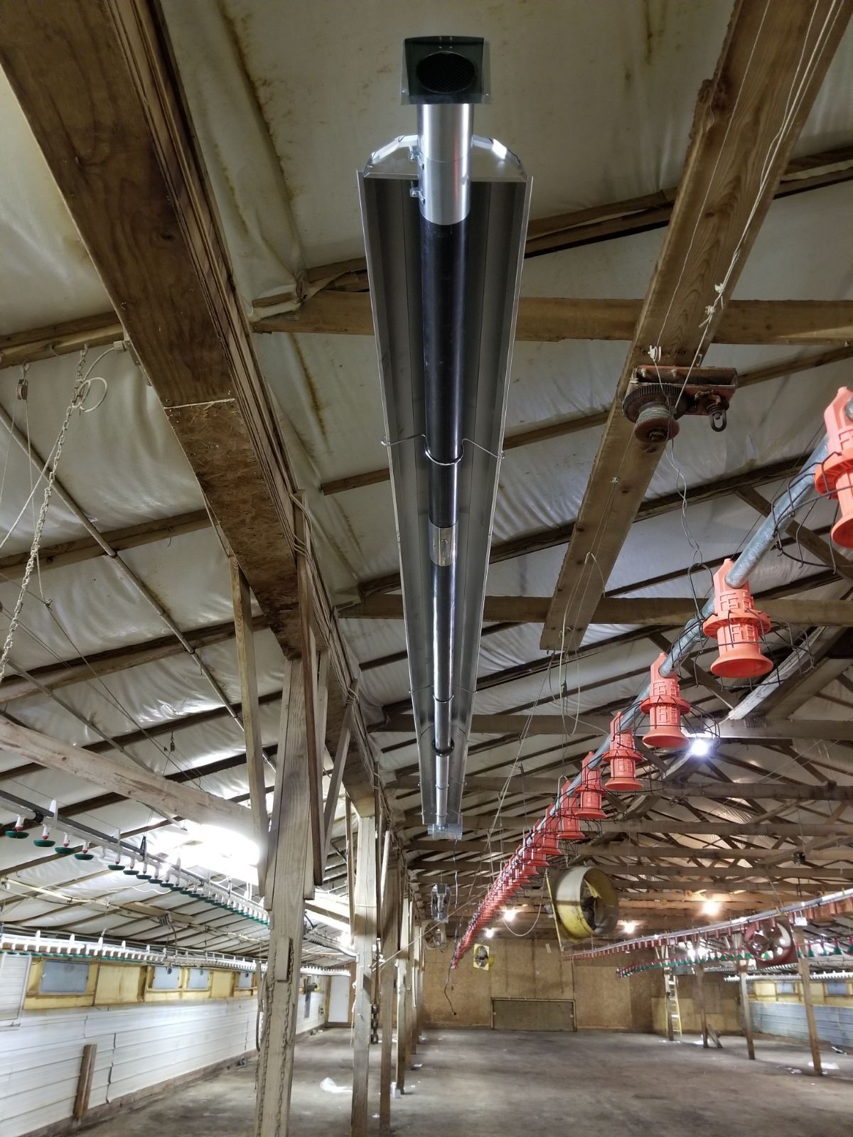Long black ventilation duct hanging from a barn-style ceiling with exposed beams and red lights.
