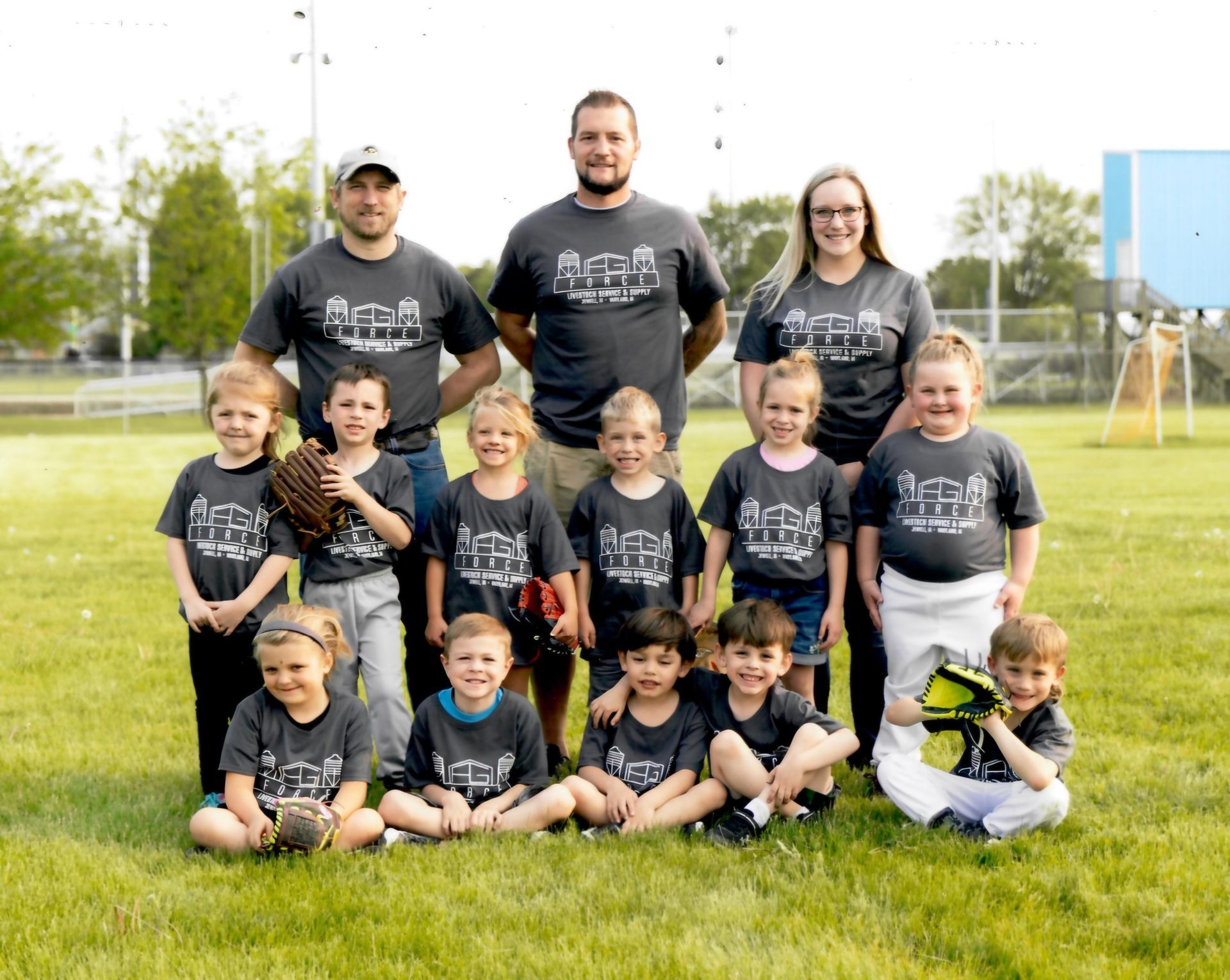Youth sports team group photo on a grassy field, wearing matching dark shirts, with coaches behind them.