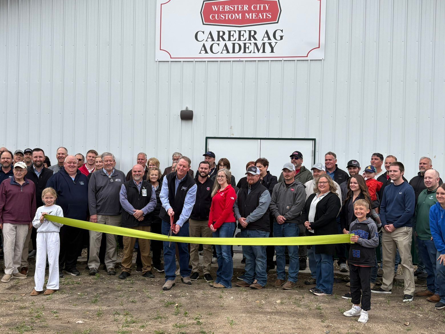 Crowd outside Carter Ag Academy holds a yellow ribbon at a ribbon-cutting ceremony