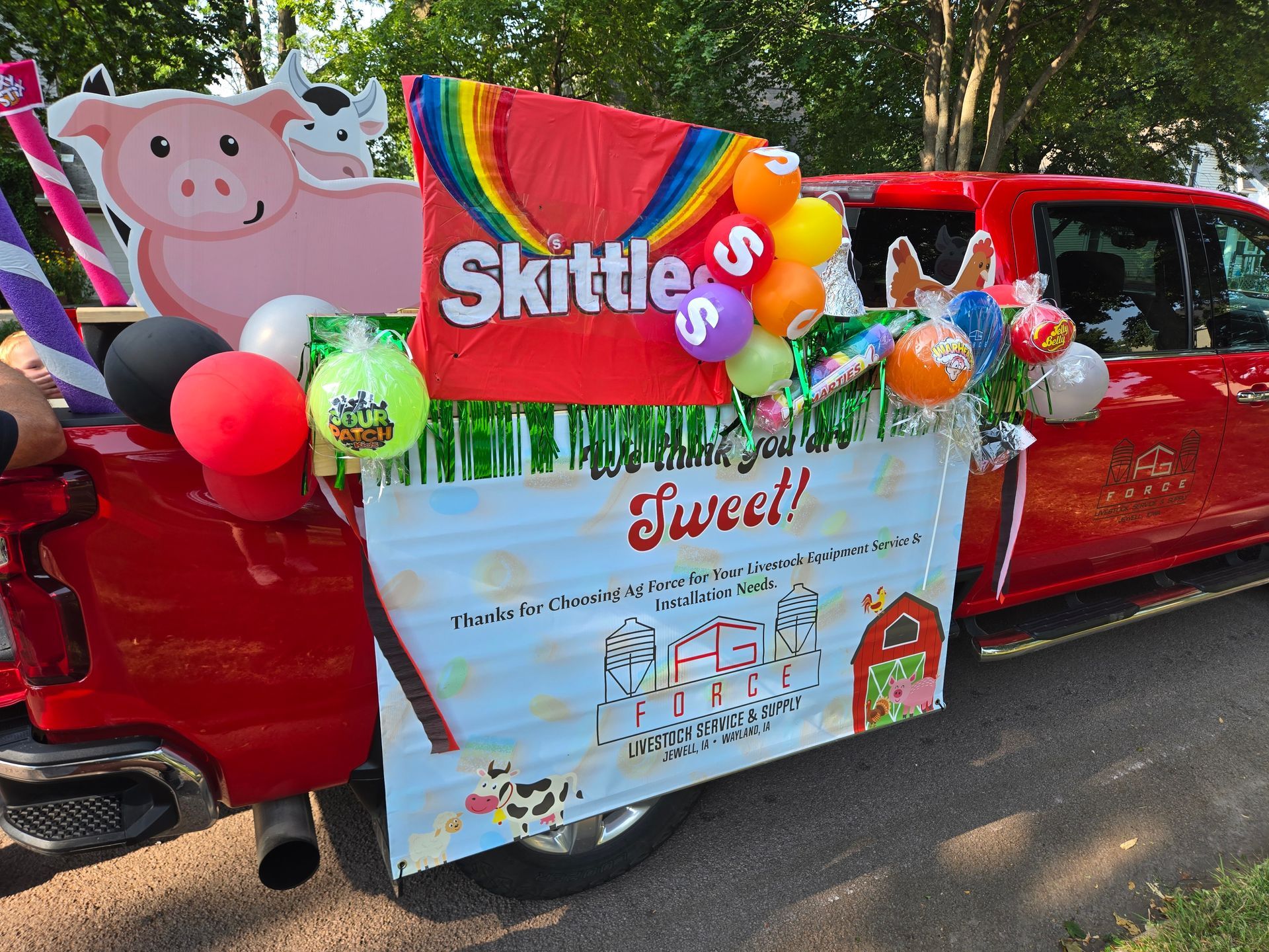 Red truck decorated with a Skittles banner, balloons, and candy-themed signs at an outdoor event