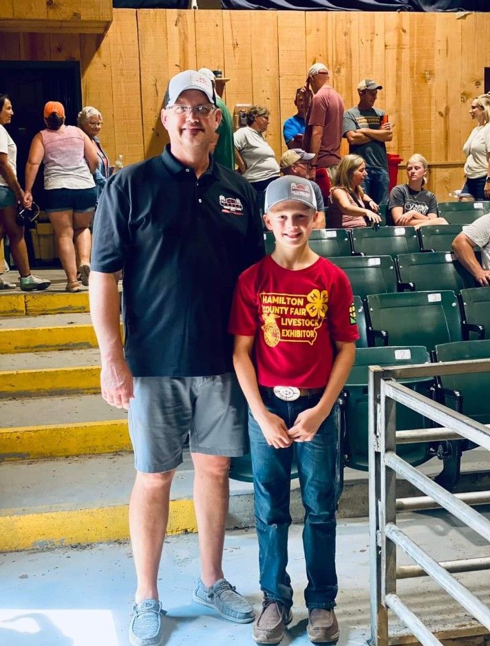 Two people standing together in a stadium aisle with green bleachers and spectators behind them