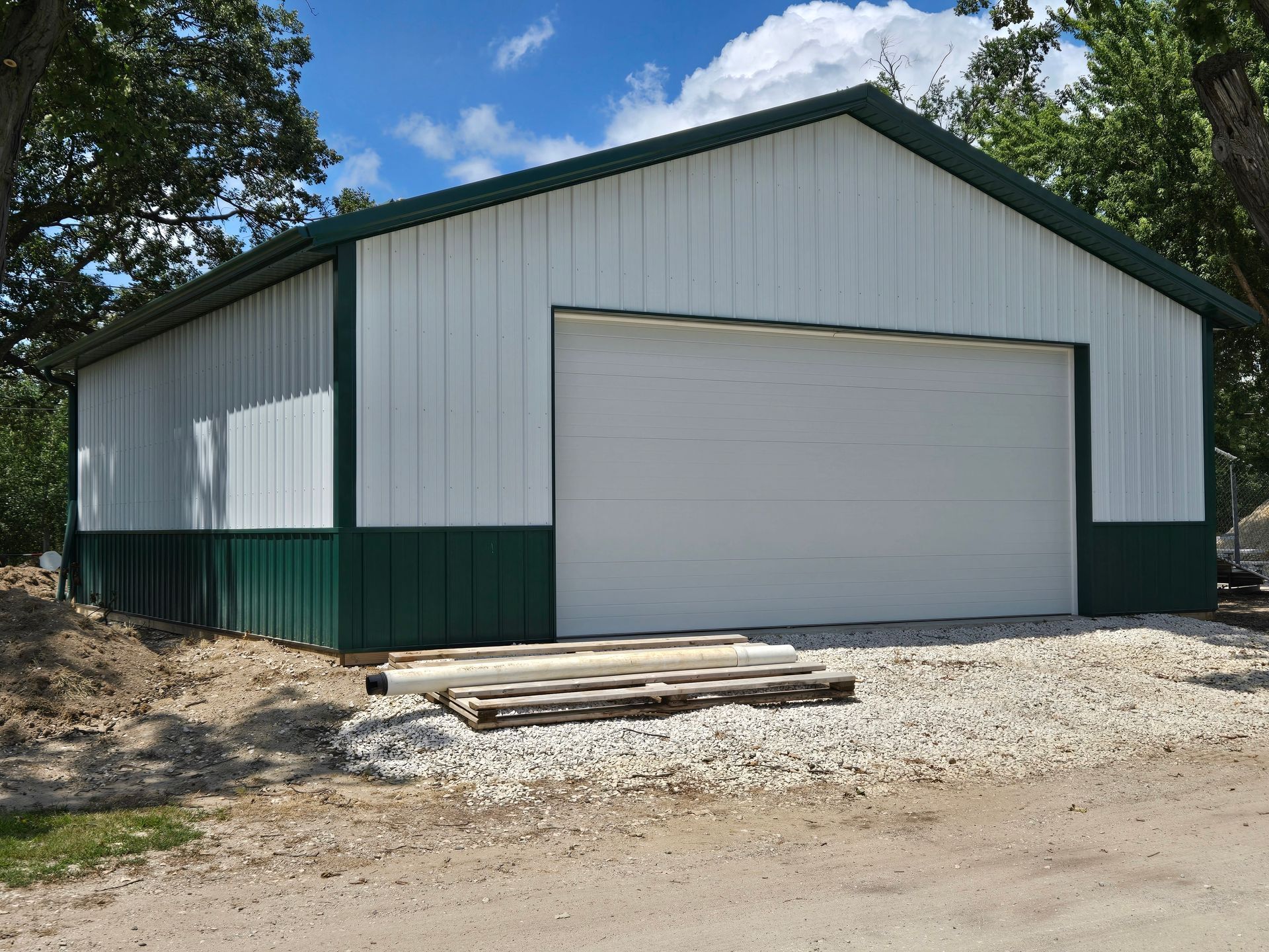 White metal garage with green trim and a large closed door on a gravel lot.