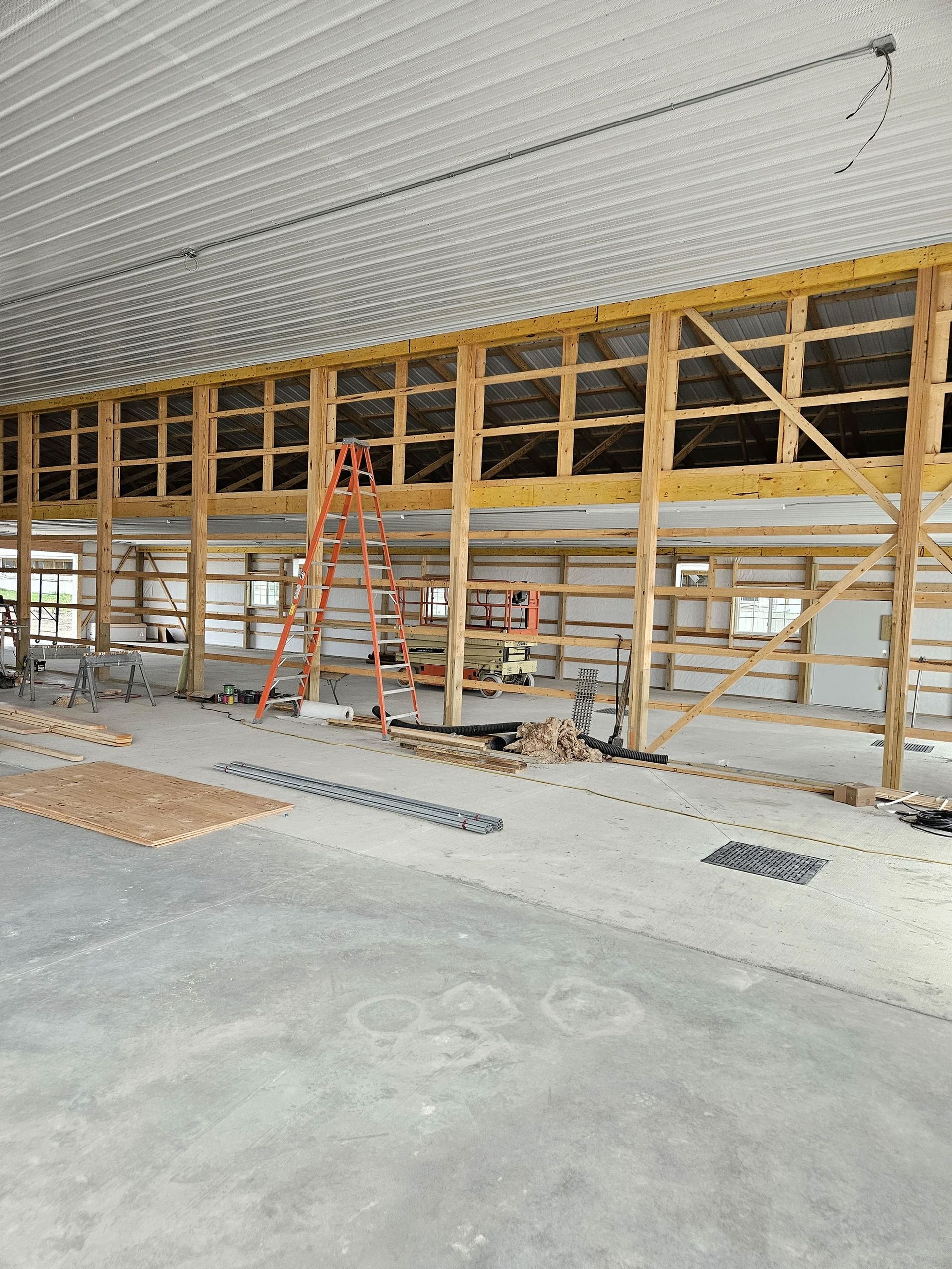 Interior of a building under construction with wooden framing, ladders, and tools along a wall