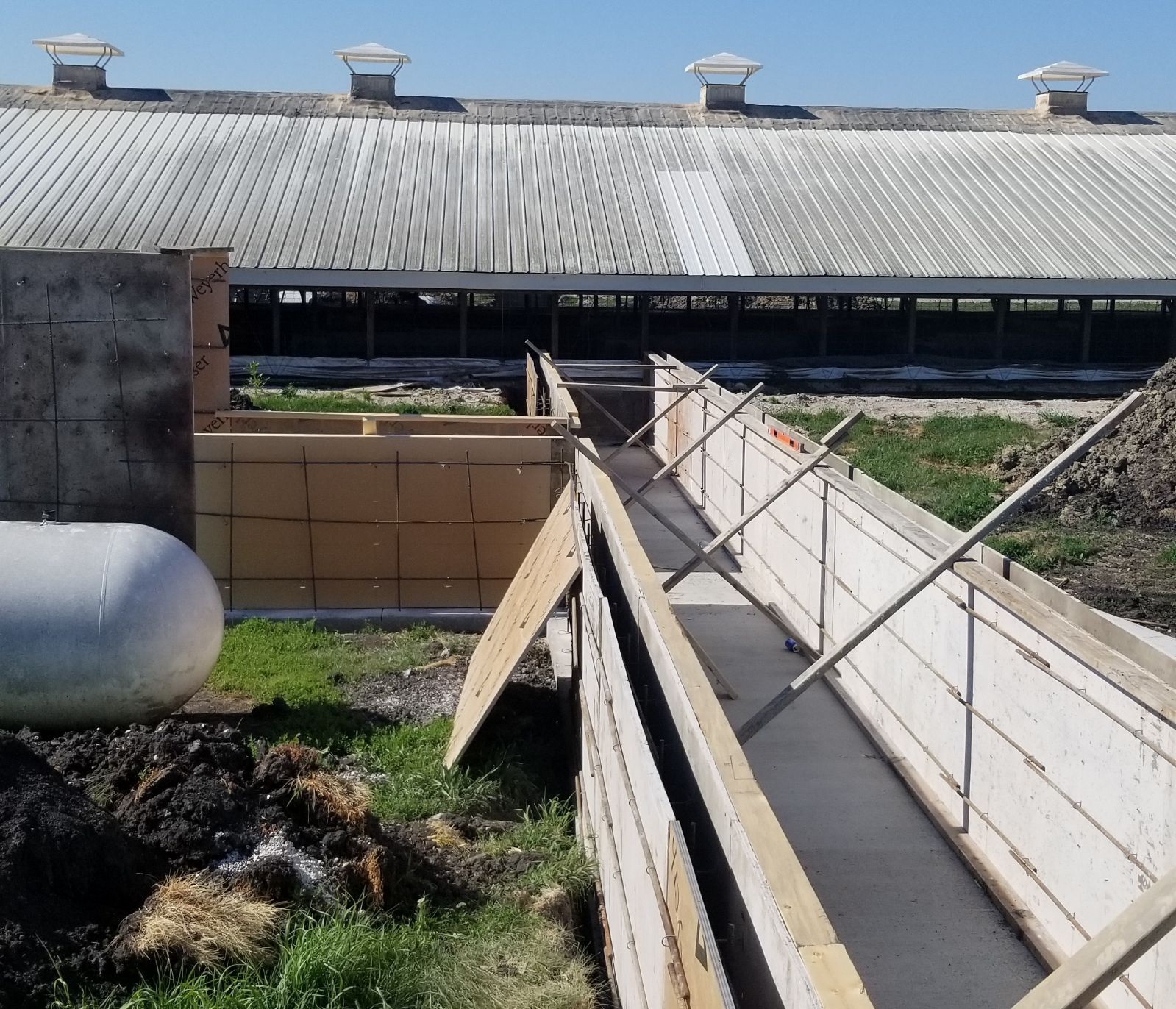 Ramped walkway beside a large barn, with white walls, metal rails, and open yard in bright sunlight