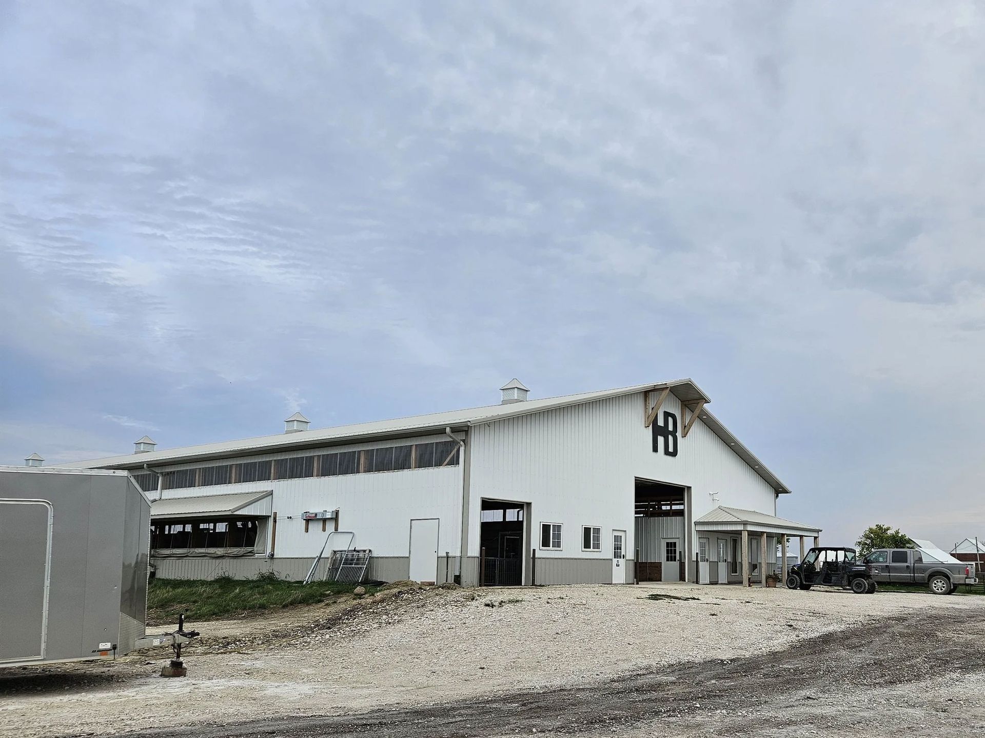 White warehouse-style building with gravel lot under a cloudy sky, with a parked truck on the right.