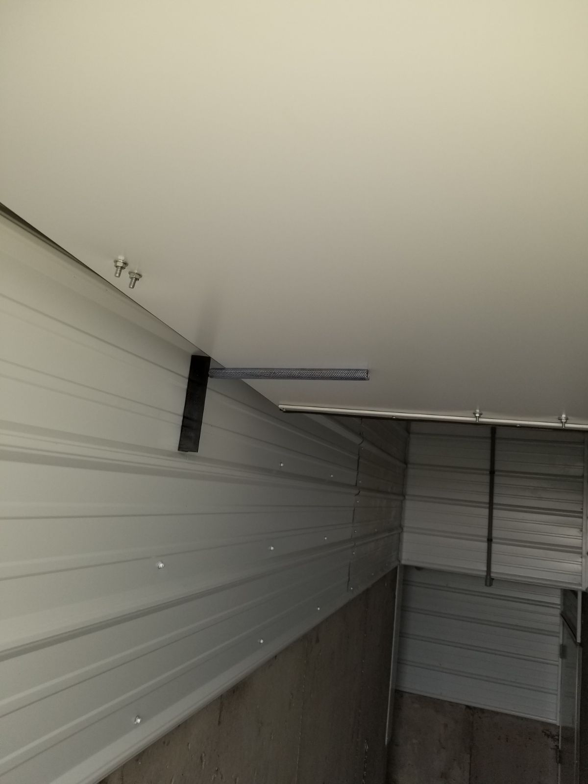 Garage wall with a black metal bracket near the ceiling and a partially open door or panel on the right.