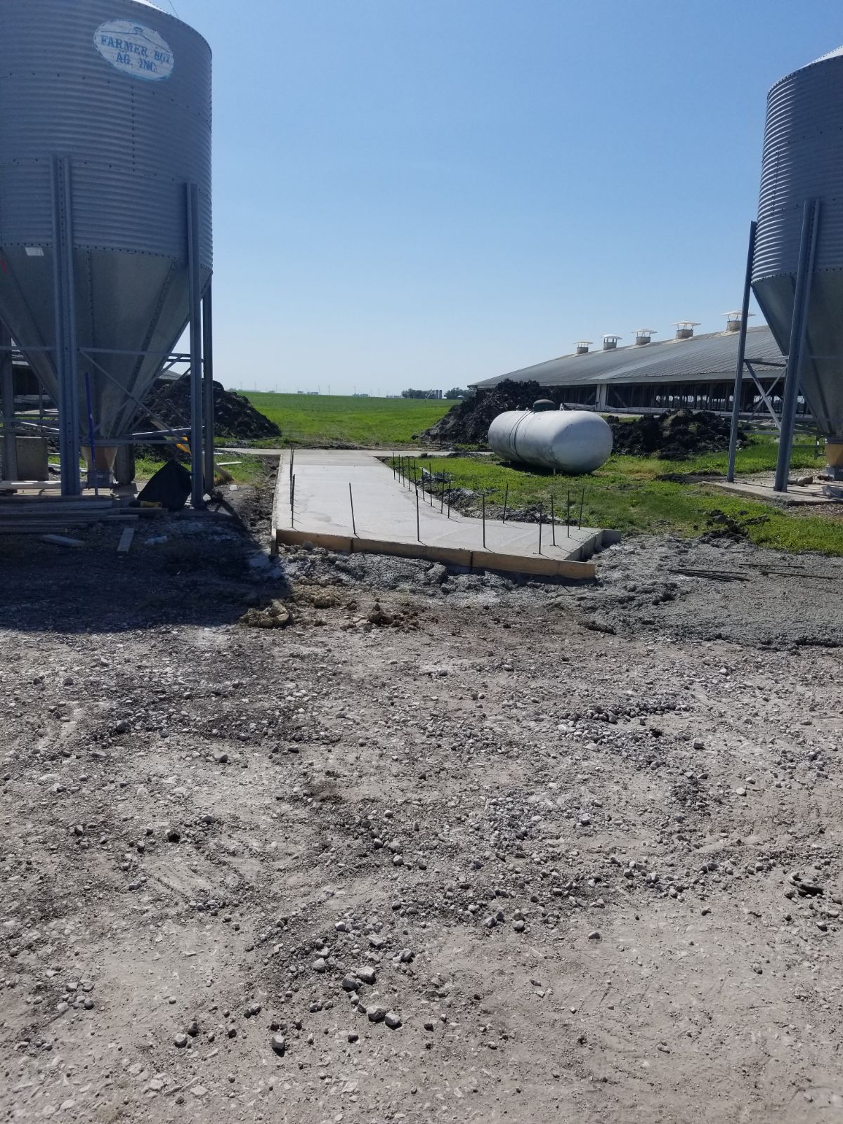 Farmyard with two grain silos, a concrete trough, and a metal livestock shed under a clear blue sky