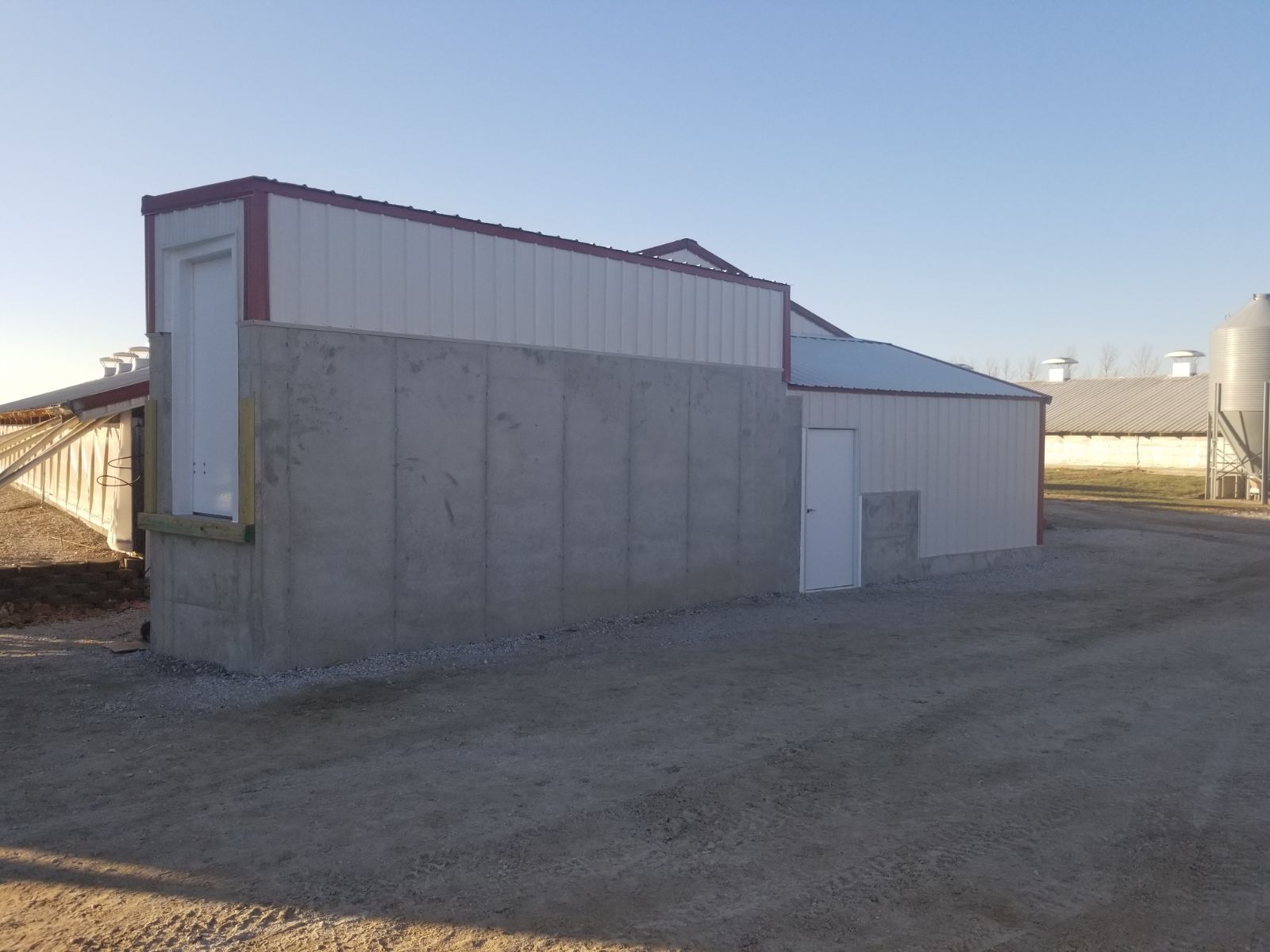 Small gray utility building with a white door and corrugated metal roof in an empty yard.