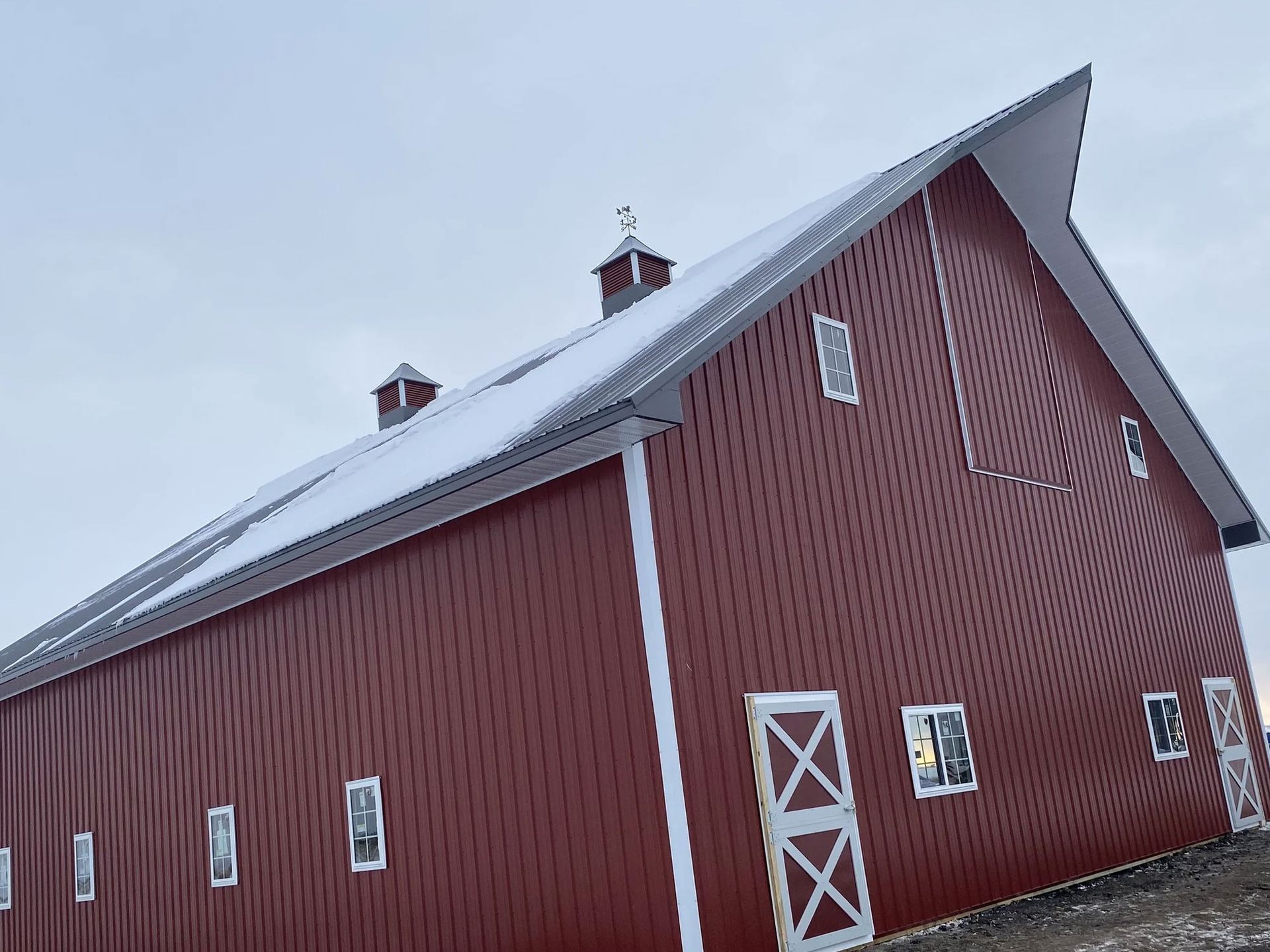 Red barn with white trim and a snow-covered roof under an overcast sky.